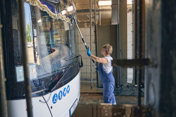 Attentive strong female person washing windshield of bus