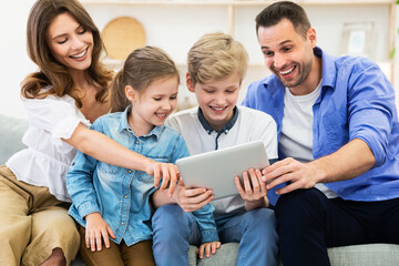 Excited Family Using Digital Tablet Sitting On Sofa Indoors