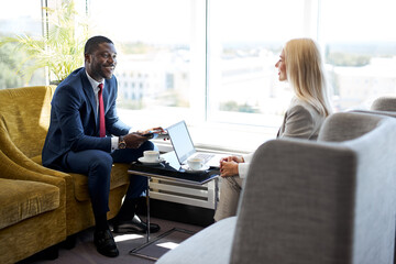 business partners have conversation in lobby of hotel, african and caucasian people talk, discuss,...