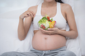 care about unborn child. pregnancy, healthy food and people concept, happy pregnant woman eating vegetable salad for breakfast sitting on bed at home. pregnancy and healthy organic nutrition.