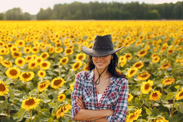 Young woman agronomist wearing cowboy hat, plaid shirt and jeans on sunflower field. Rich harvest concept