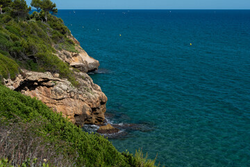 View of the beautiful blue Mediterranean sea with rocks near the shore with waves on a sunny day