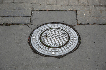 Metal manhole cover on rough cobblestone and asphalt street