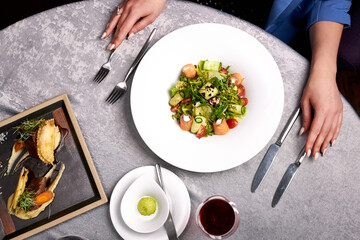 top view on cropped woman going to try delicious restaurant food, salad from fresh vegetables, glass of red wine and meat for guests