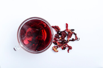 Top view of glass cup of hot hibiscus tea and dried petals on the white surface