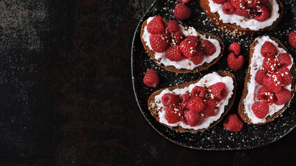 Raspberry bruschetta on a plate on a dark surface. Open sandwiches with raspberries and cream cheese. Healthy snack. Vegetarian diet. Keto diet.