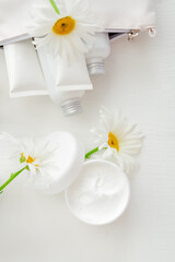 Moisturizer skin cream in white jar with chamomile flowers. Mockup white plastic jar for moisturizer skin cream, lotion on white background. Set white skin care products in tubes and bottles.Top view