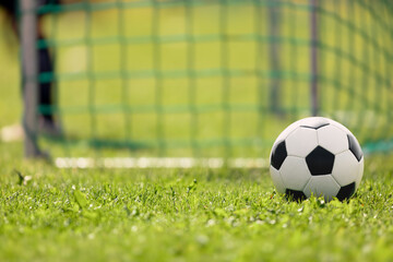 Soccer ball on the grass of football field. Soccer goal and goalkeeper in a blurred background.