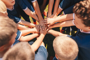 Happy kids sports team stacking hands at the field. Children team sports. Boys at sports camp...