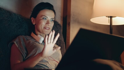 Woman starting video call on laptop. Girl waving hand to notebook camera on sofa