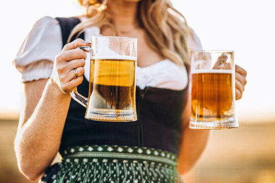 Close-up photo of blonde in dirndl, traditional festival dress, holding two mugs of beer in her hands