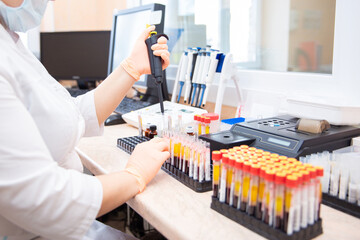 hands of a lab technician with a tube of blood sample and a rack with other samples / lab technician holding blood tube sample for study