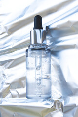 glass bottle with pipette with skin care serum on a silver aluminum foil