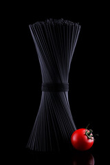 Black spaghetti with red tomato on black background
