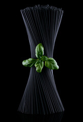 Black spaghetti with basel leaves on black background