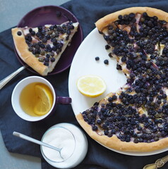 Homemade baking.Summer cake with nightshade and apples, drenched in beaten eggs with a cup of tea and a fork on a gray wooden table. View from above.