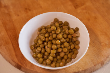 white plate with canned green peas on a wooden background