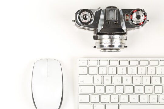 Retro analog SLR camera next to computer keyboard and mouse on white background, digital photography or image processing concept, flat lay top view from above