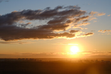 Beautiful sunset of a large orange sun behind summer clouds in a dark sky