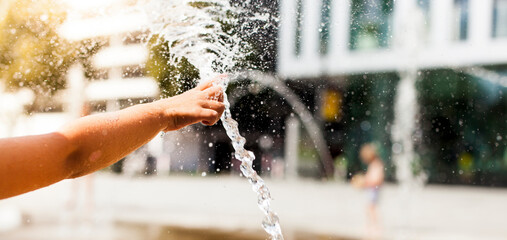 Kind spielt mit Wasser in der Stadt. Abkühlung im urbanem Raum für Bewohner. Architektur der...