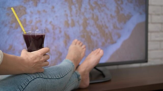 Enjoy the sea image. A woman with a glass of juice enjoys the view of the sea on the TV.