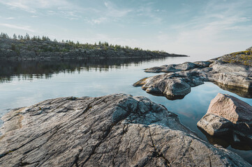 Sunrise on a rocky shore. Still water. Pine forest in the background.