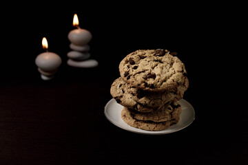 Zen Pile of chocolate cookies with stone piles in the back topped with candles on a dark environment