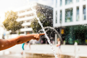 Child seeks cooling off with water in the city. Heat spell in the city. Kind sucht Abkühlung mit...