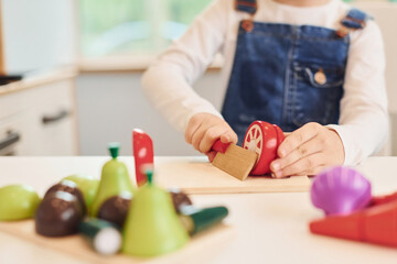 Close up view of little girl in casual clothes that have fun by playing with toys on the kitchen