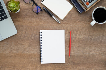 Top view above of Notebook on wood office desk table with laptop and coffee cup with equipment other office supplies. 