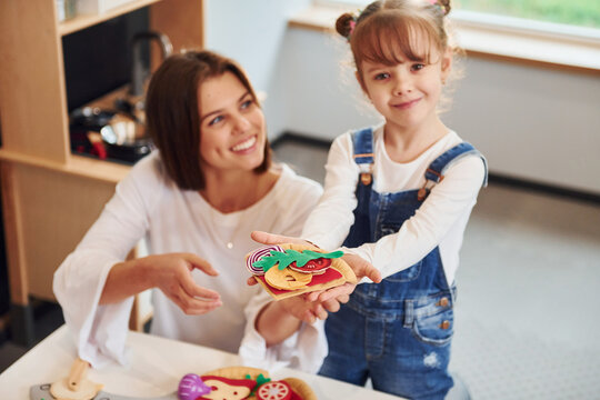 Young woman with little girl playing with toys together on the kitchen