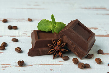 Two pieces of chocolate with star anise, mint and coffee grains on white wooden Provence style table