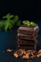 Heap of chocolate pieces with mint on dark wooden table.