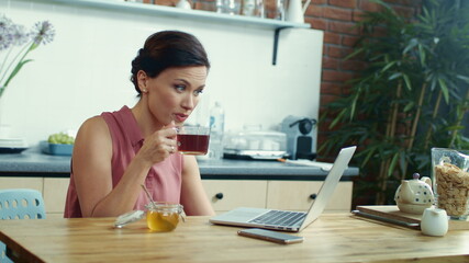Business woman chatting online on laptop. Girl drinking tea during online call.