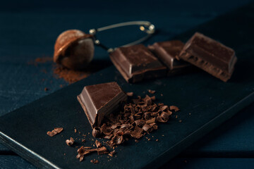 Pieces of chocolate, chocolate shavings and strainer with cocoa on dark wooden table