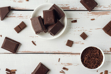 Pieces of chocolate with chocolate shavings on white Provence style table. Top view. Flat lay. Copy...