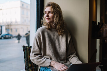 Pensive young lady looking through window on town