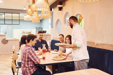 Chef delivers food. Group of young friends that sitting together indoors and eating pizza