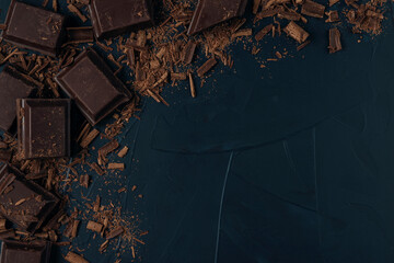Pieces of chocolate with chocolate shavings on dark blue textured background. Flat lay. Copy space.