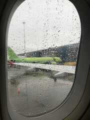 The blurred wing of the plane is visible through a drop of rain on the window of the aircraft