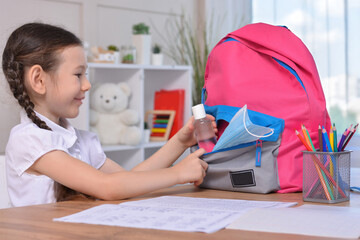 Schoolgirl puts sanitizer and mask into her backpack.Student safety after covid-19 pandemic. Back to school after coronavirus outbreak.Virus and disease prevention for kids.