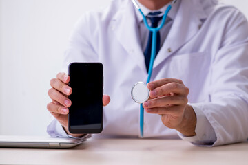 Young male doctor with stethoscope repairing computer