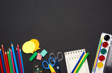 colorful wooden pencils, scissors, notepads and paint for drawing on a blank black chalk board