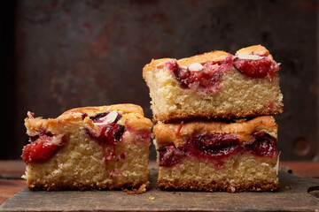 stack of square baked sponge cake slices with plums on wooden kitchen board