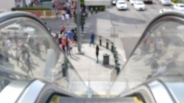 Perspective view thru escalator, defocused unrecognizable group of people on road intersection crosswalk on Strip of Las Vegas, USA. Anonymous blurred pedestrians on walkway in crowded urban downtown.