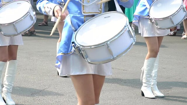 Street performance of festive march of drummers girls in blue costumes on city street. Close-up of female hands drummers are knocking in the drum of their sticks
