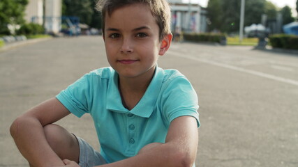Cute boy sitting in amusement park. Close up relaxed teen boy outside