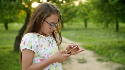 Serious girl playing games on phone. Concentrated girl standing in summer park