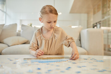 Obraz na płótnie Canvas Warm-toned portrait of cute little girl solving jigsaw puzzle while enjoying time indoors at home, copy space