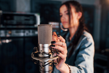 Close up view of microphone. Young beautiful female performer rehearsing in a recording studio